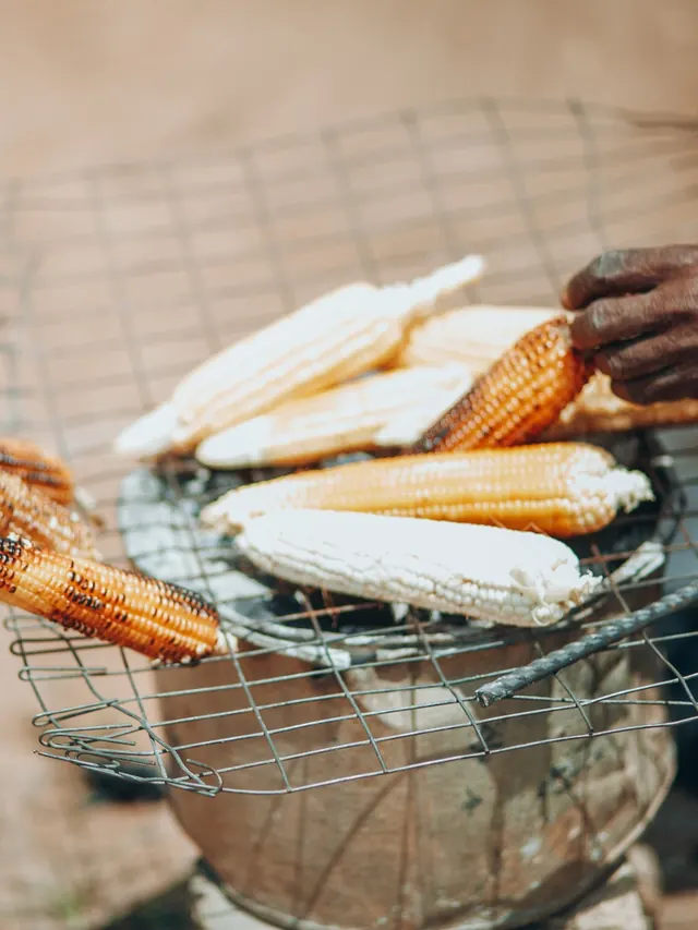An elderly cook's hands turning roasting maize