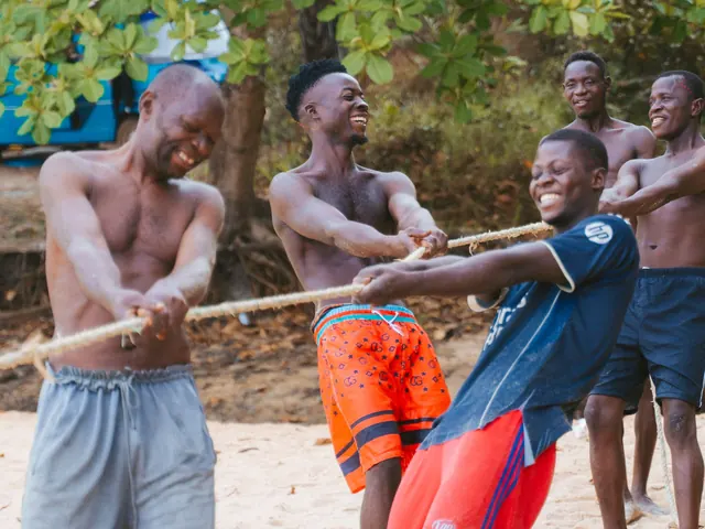Young men laugh as they pull hard in a tug of war on the beach