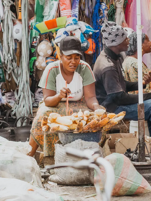A vendor roasts maize over charcoal at a market stall