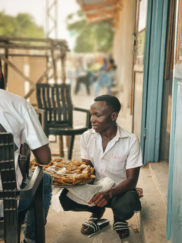 A street vendor serves fried snacks to a seated customer